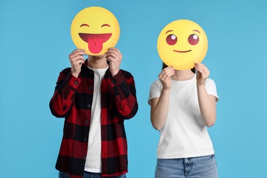 People covering faces with emoticons on light blue background