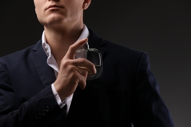 Photo of Handsome man in suit using perfume on dark background, closeup