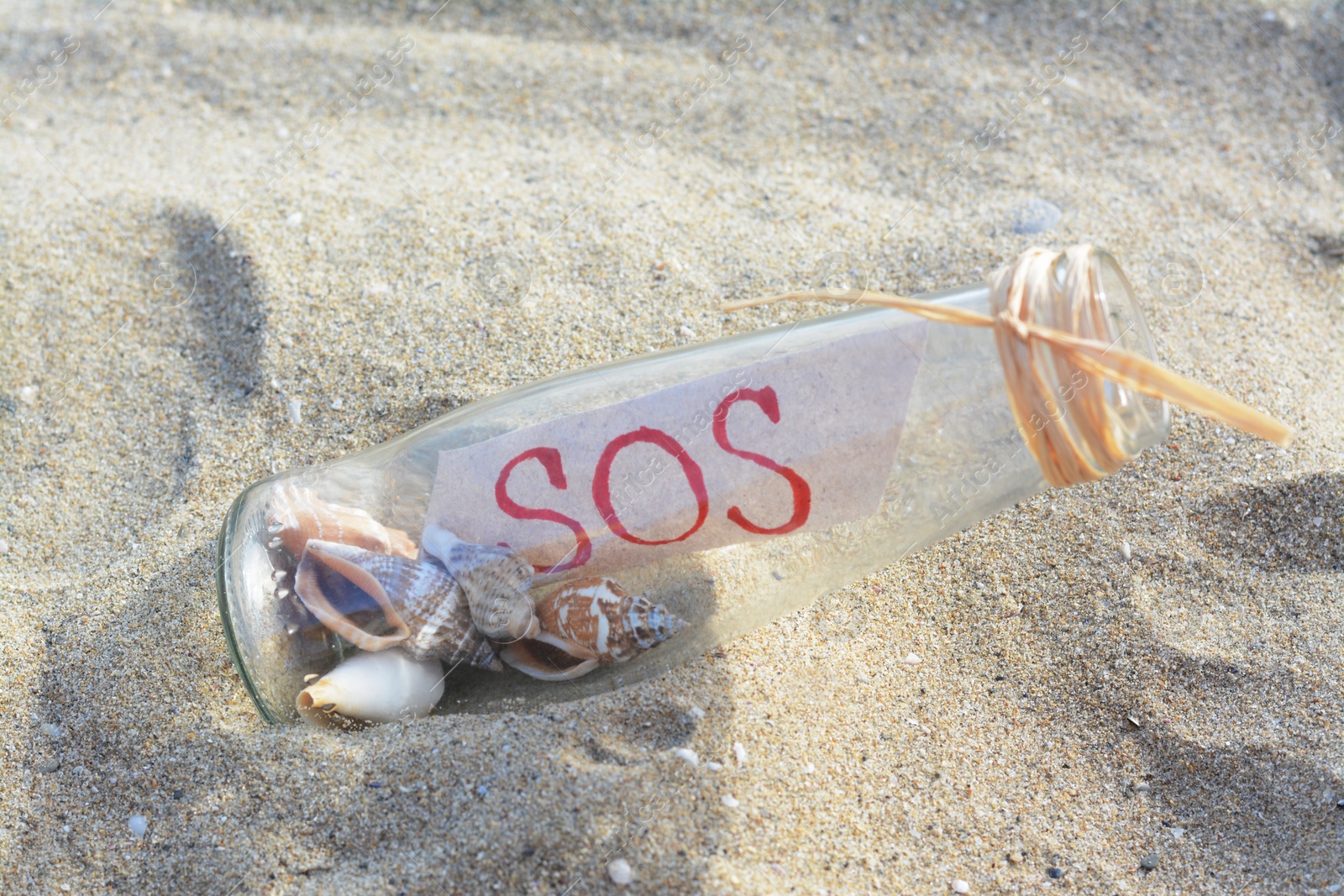 Photo of Glass bottle with seashells and message SOS on sand, closeup