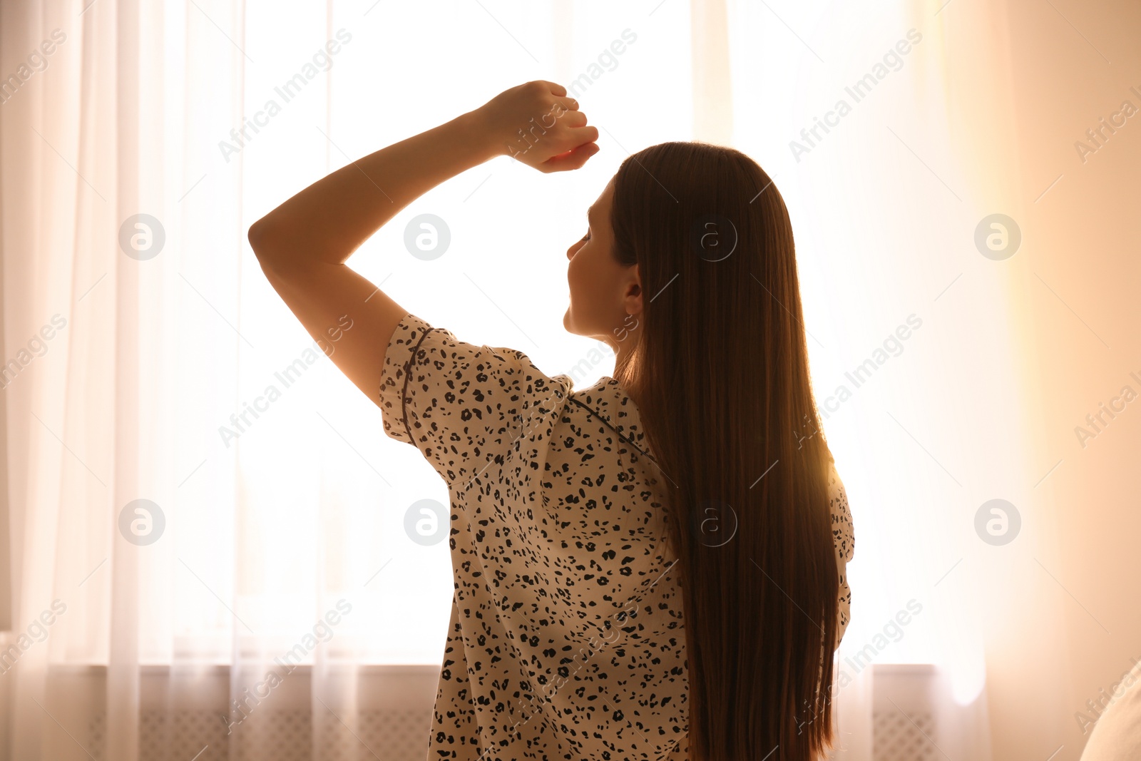 Photo of Young woman stretching near window at home. Lazy morning