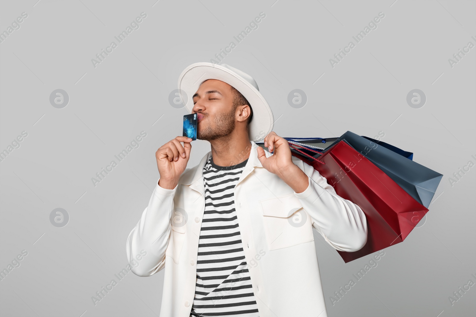 Photo of Happy African American man in hat with shopping bags and credit card on light grey background