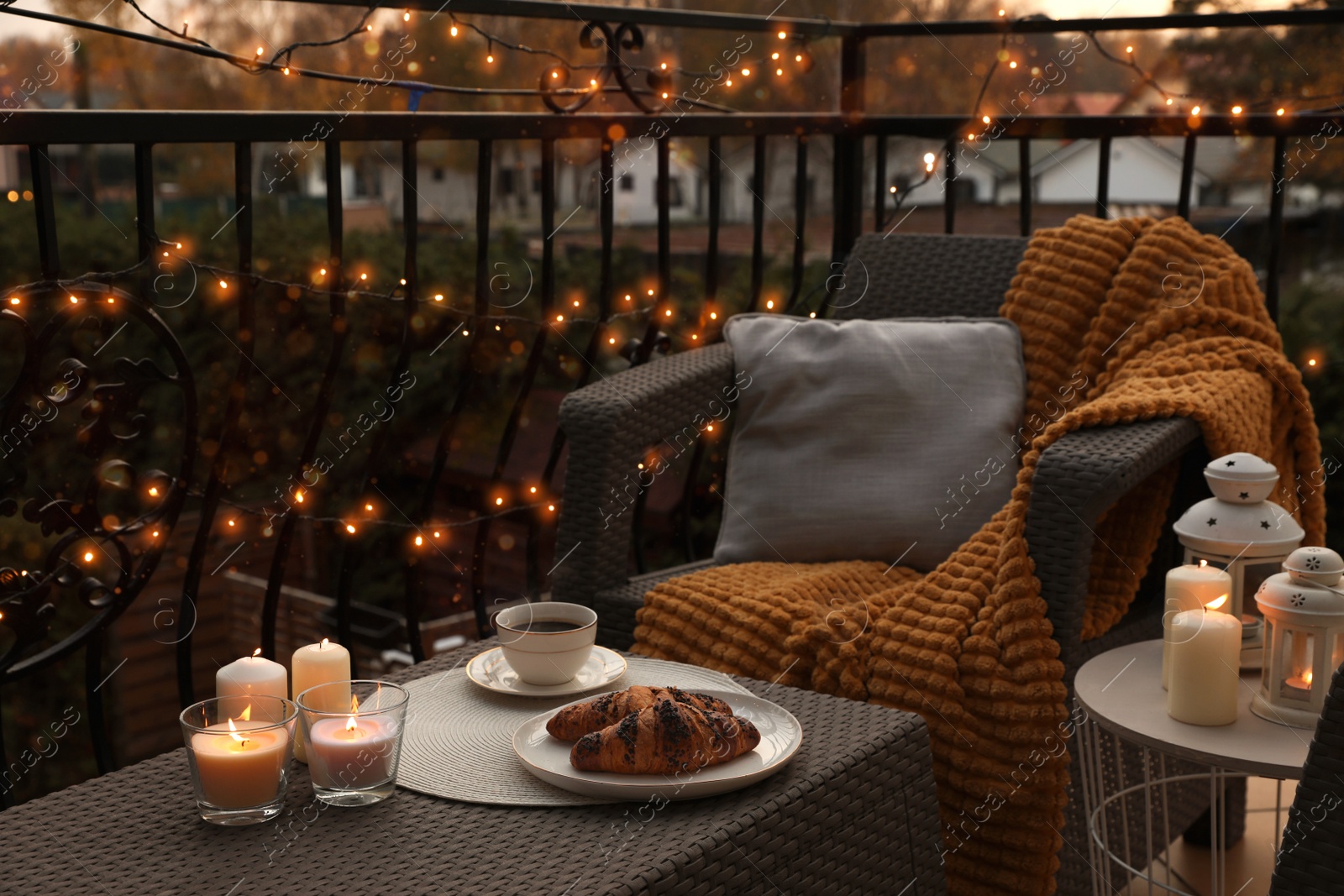 Photo of Beautiful view of garden furniture with pillow, soft blanket and burning candles at balcony