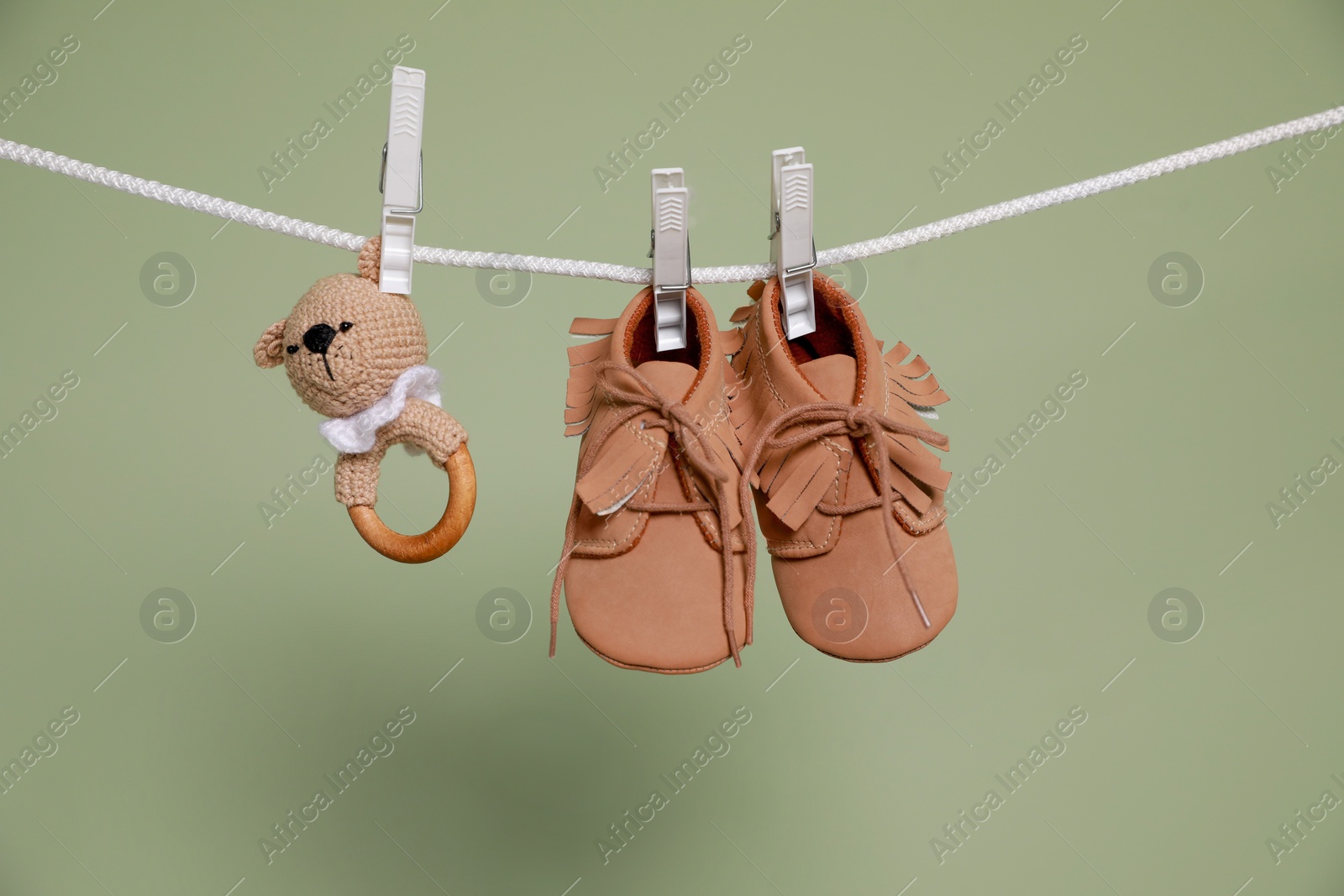 Photo of Cute small baby shoes and toy hanging on washing line against green background