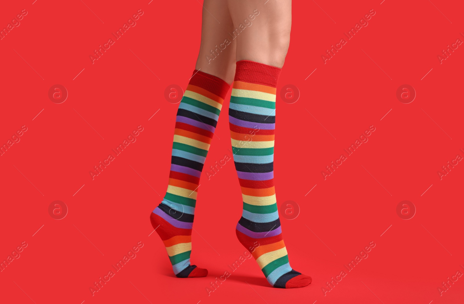 Photo of Woman in stylish rainbow socks on red background, closeup