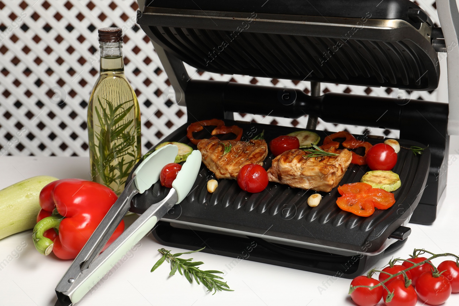 Photo of Electric grill with different products and tongs on white table