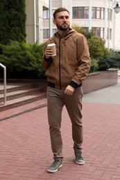 Photo of Handsome man wearing stylish clothes with cup of coffee on city street. Autumn walk