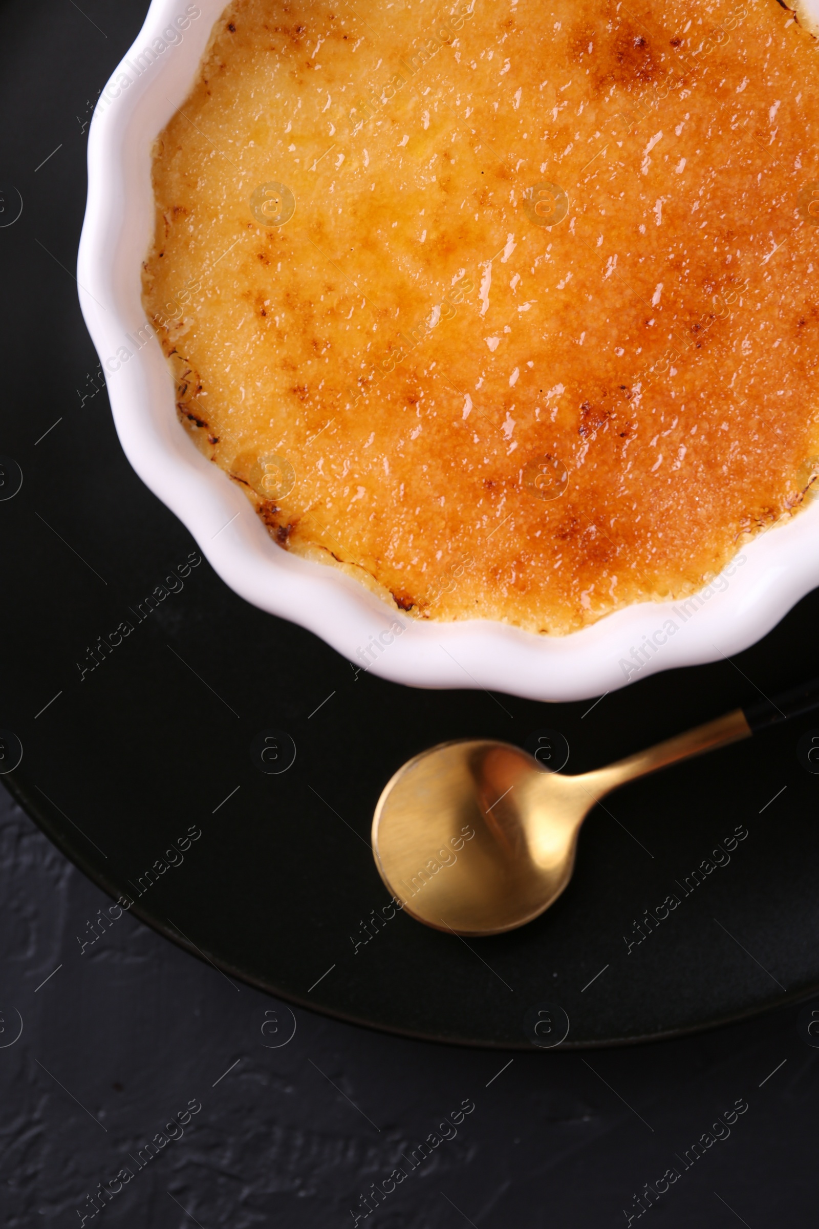 Photo of Delicious creme brulee in bowl served on dark gray textured table, top view