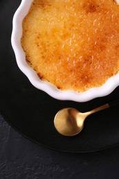 Photo of Delicious creme brulee in bowl served on dark gray textured table, top view