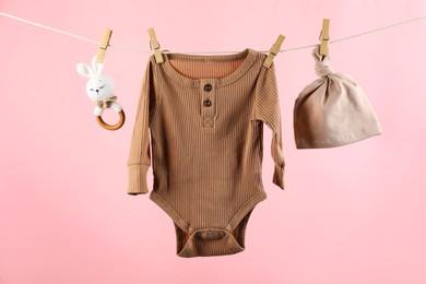 Baby clothes and accessories hanging on washing line against pink background