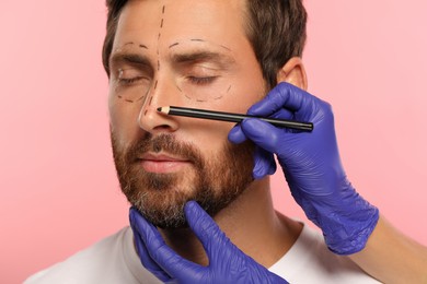 Photo of Doctor with pencil preparing patient for cosmetic surgery operation on pink background, closeup