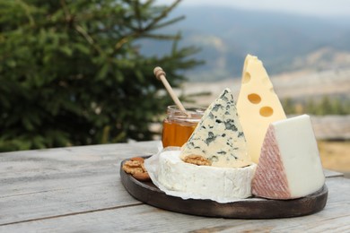 Different types of delicious cheeses on wooden table against mountain landscape. Space for text