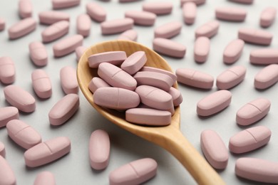 Photo of Vitamin pills and wooden spoon on light grey background, closeup. Health supplement