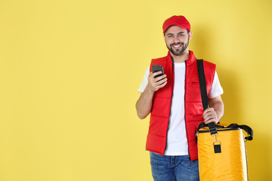 Photo of Courier with thermo bag and mobile phone on yellow background, space for text. Food delivery service