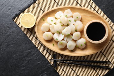 Photo of Raw scallops with green onion, soy sauce and lemon on dark textured table, top view