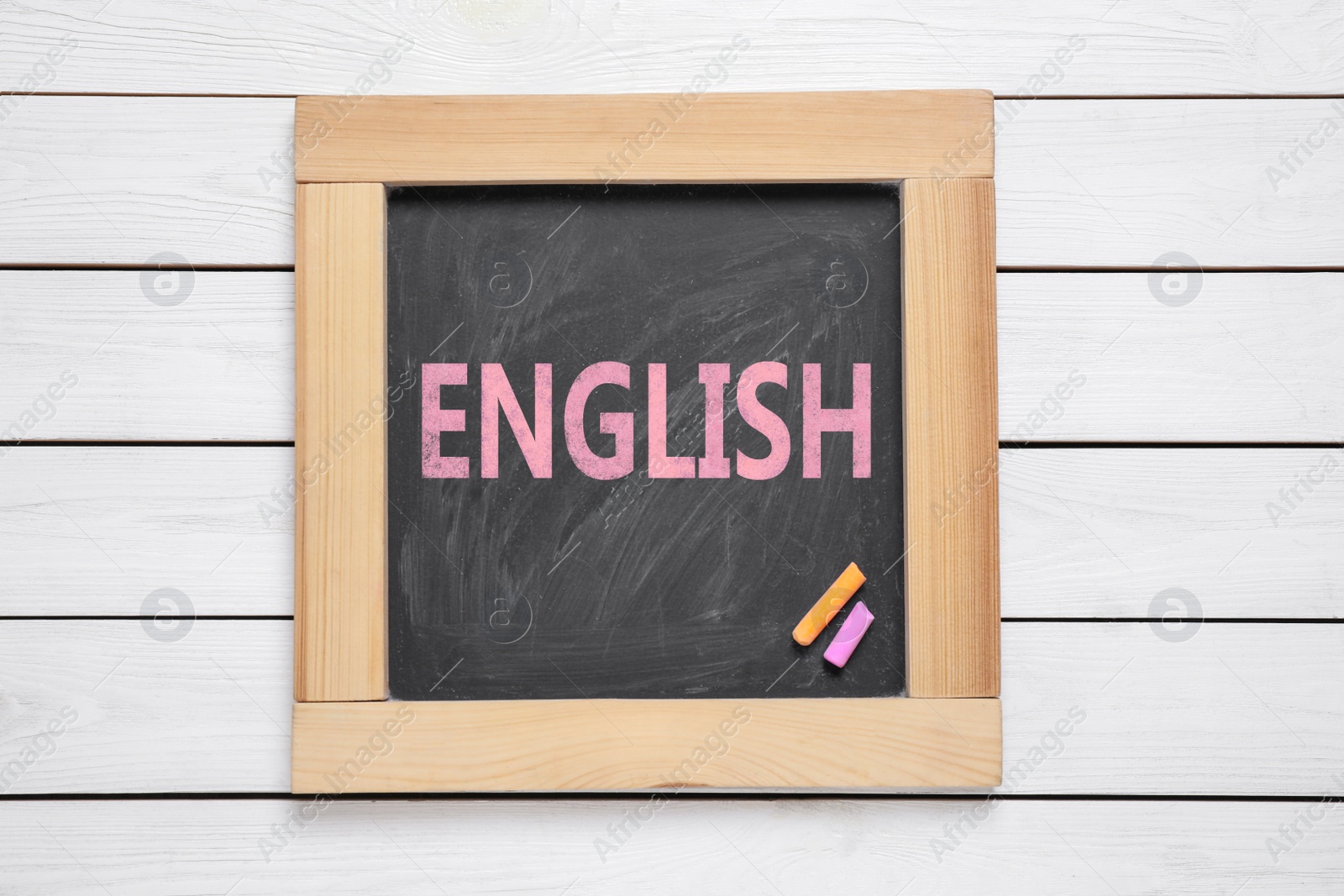 Image of Blackboard with word ENGLISH and pieces of color chalk on white wooden background, top view