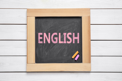 Blackboard with word ENGLISH and pieces of color chalk on white wooden background, top view