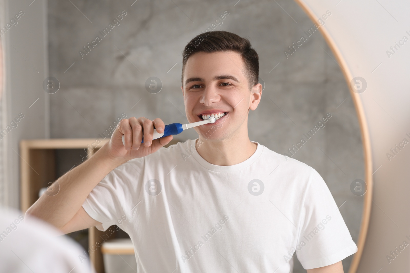 Photo of Man brushing his teeth with electric toothbrush near mirror in bathroom