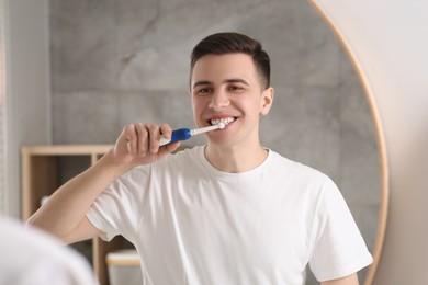 Man brushing his teeth with electric toothbrush near mirror in bathroom