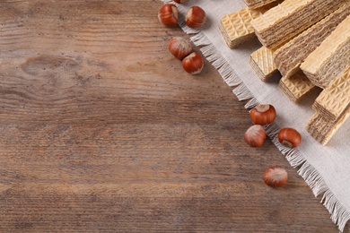 Photo of Delicious wafers with hazelnuts on brown wooden background, top view. Space for text