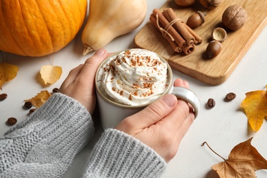 Woman holding cup with tasty pumpkin spice latte at light table, closeup