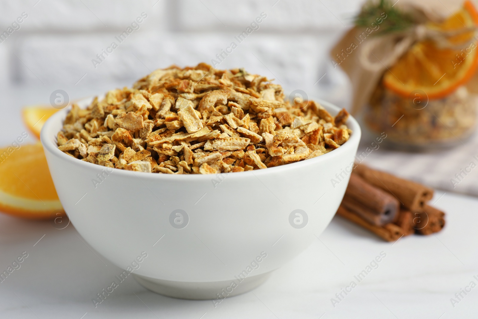 Photo of Bowl of dried orange zest seasoning, fresh fruit and cinnamon on white marble table