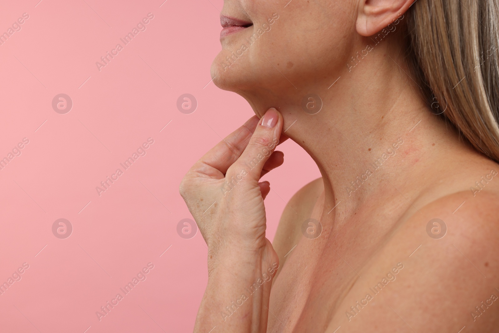 Photo of Mature woman touching her neck on pink background, closeup. Space for text