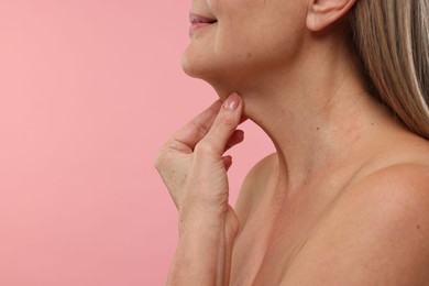 Photo of Mature woman touching her neck on pink background, closeup. Space for text