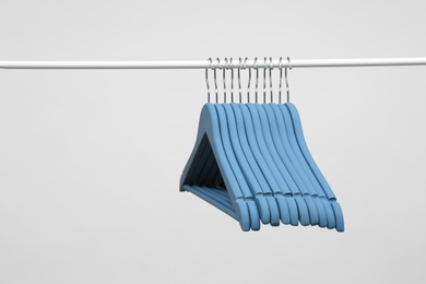 Empty clothes hangers on metal rail against light background. Space for text