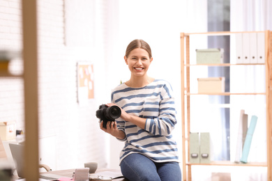Photo of Young journalist with camera at workplace in light office