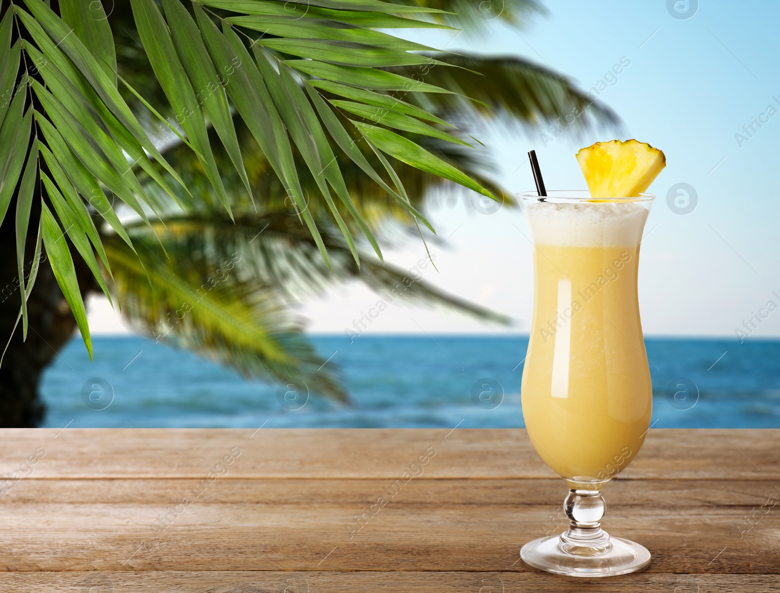 Image of Tasty pineapple cocktail in glass on wooden table at beach, space for text