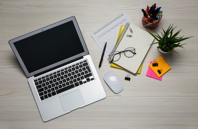 Modern laptop, glasses and office stationery on white wooden table, flat lay. Distance learning