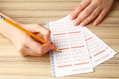 Photo of Woman filling out lottery tickets with pencil on wooden table, closeup