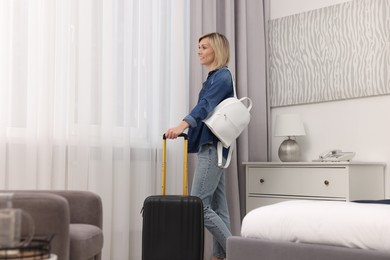 Photo of Smiling guest with suitcase and backpack exploring stylish hotel room