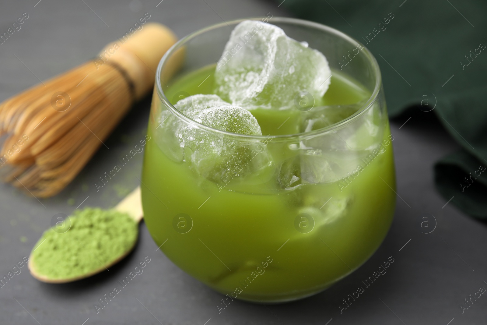 Photo of Glass of delicious iced green matcha tea and powder on grey table, closeup