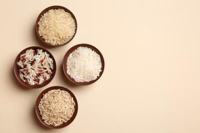 Flat lay composition with brown and other types of rice in bowls on light background, space for text