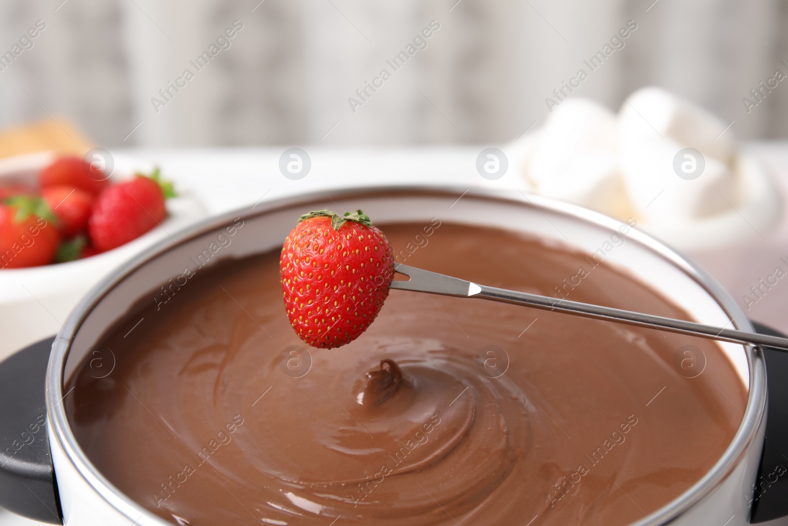 Photo of Dipping strawberry into pot with chocolate fondue on table, closeup