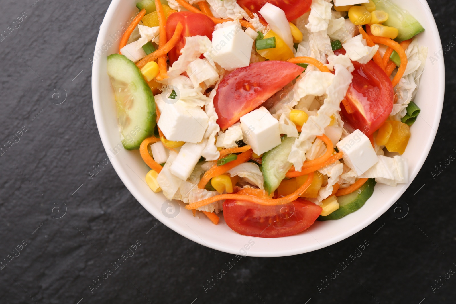 Photo of Tasty salad with Chinese cabbage, carrot, cheese, cucumber, corn and tomato on black table, top view