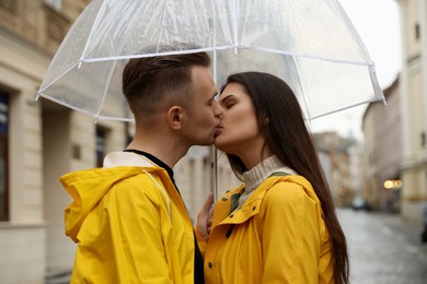 Lovely young couple with umbrella kissing on city street