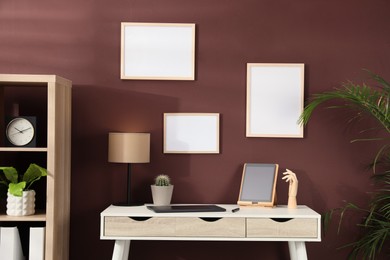 Photo of Empty frames hanging on brown wall indoors. Mockup for design