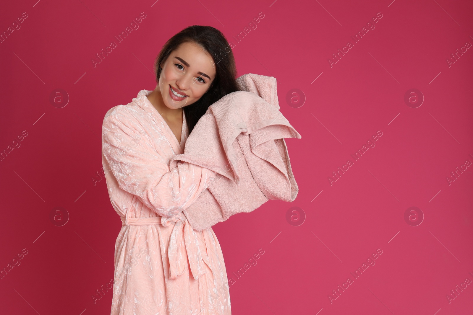 Photo of Young woman in bathrobe drying hair with towel on crimson background. Space for text