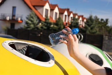 Photo of Woman throwing plastic bottle into recycling bin outdoors, closeup