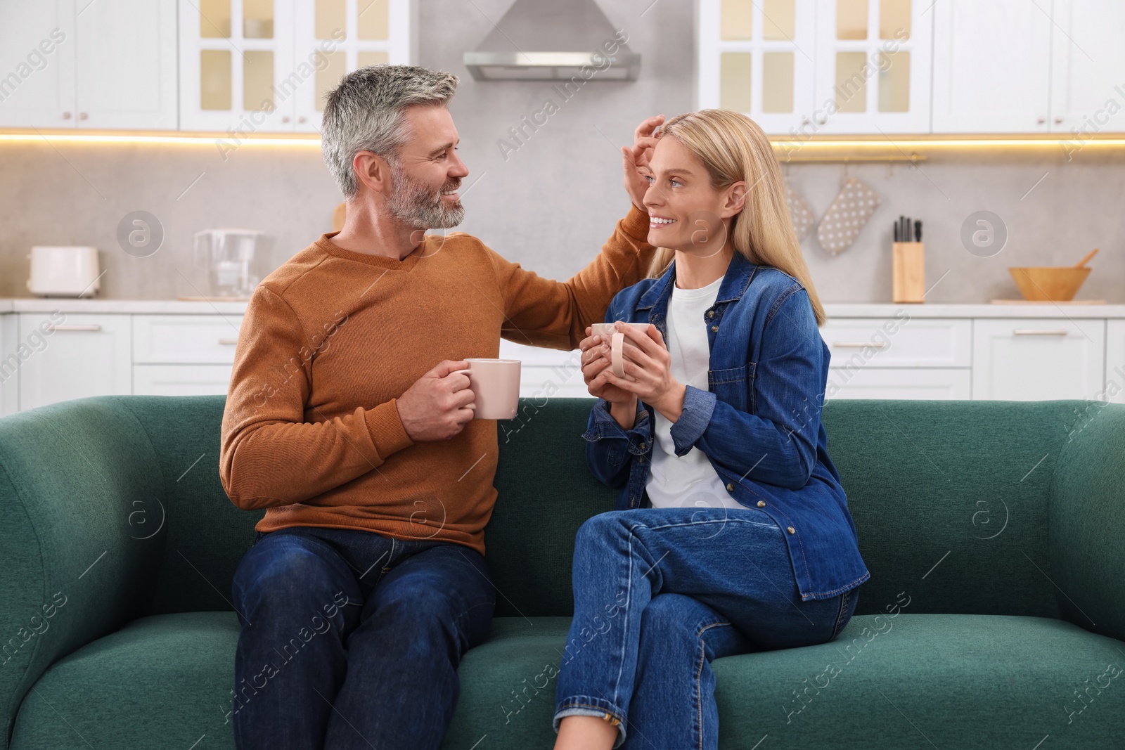 Photo of Happy affectionate couple with cups of hot drinks on sofa at home. Romantic date