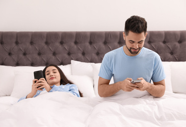 Young couple addicted to smartphones in bed at home