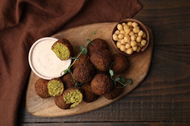 Delicious falafel balls, chickpeas and sauce on wooden table, top view