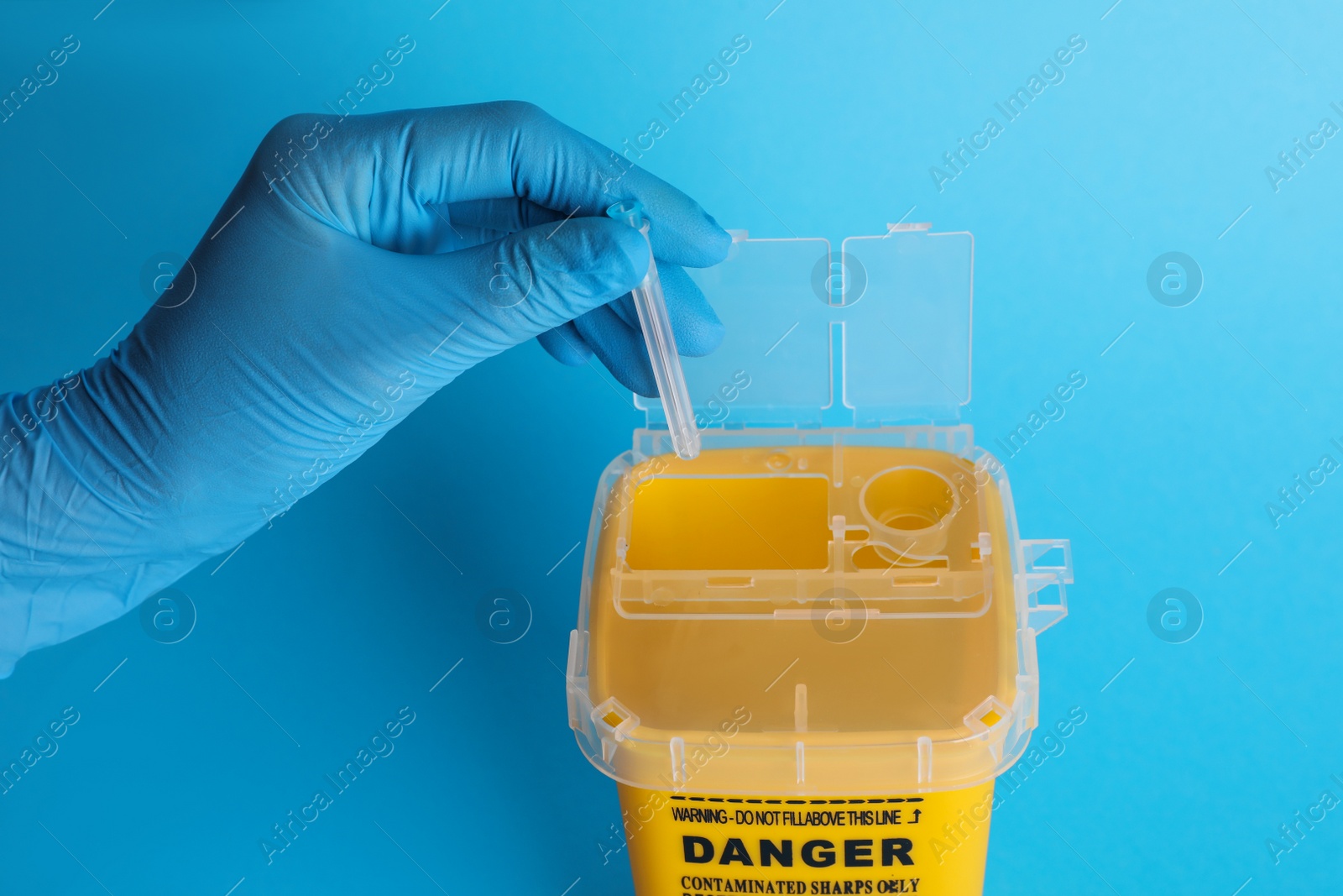 Photo of Doctor throwing used syringe needle into sharps container on light blue background, closeup