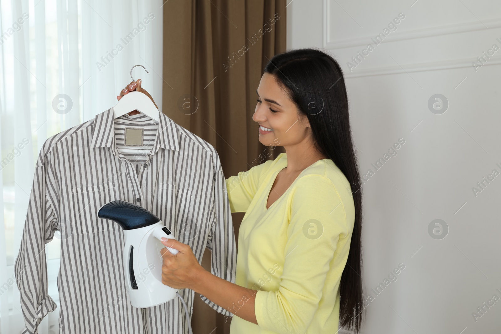 Photo of Woman steaming shirt on hanger at home