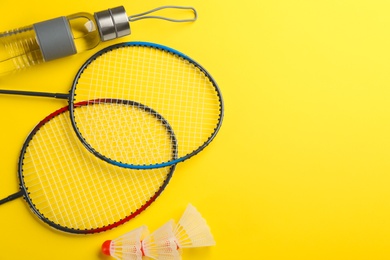 Photo of Badminton rackets, shuttlecocks and bottle yellow background, flat lay. Space for text
