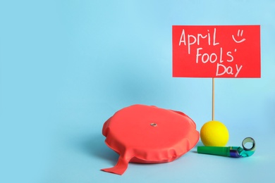 Photo of Sign with phrase Happy Fools' Day and clown's accessories on light blue background, space for text