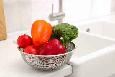 Photo of Fresh clean vegetables in colander on countertop near sink. Space for text