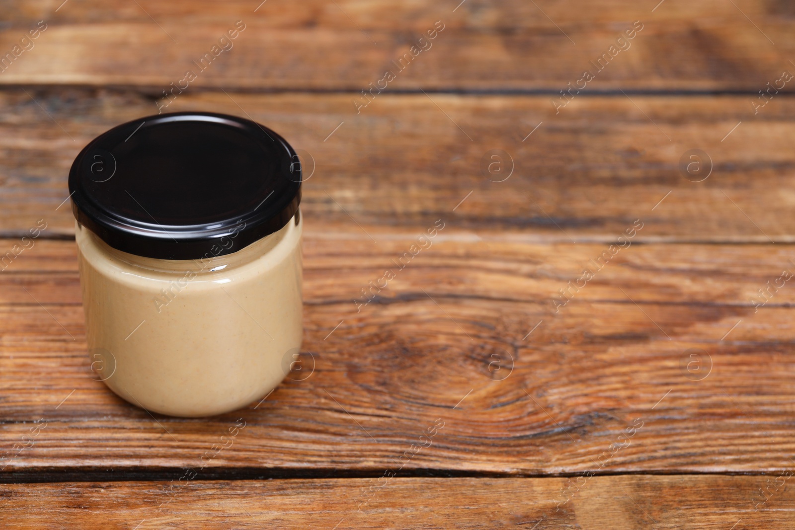 Photo of Tasty nut paste in jar on wooden table. Space for text